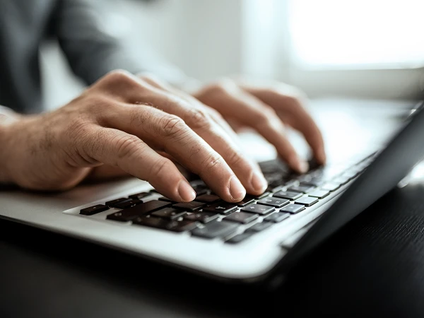 Ein Mann tippt auf der Tastatur eines MacBook, während er am Schreibtisch sitzt.